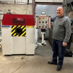 Man stands smiling next to flanging machine